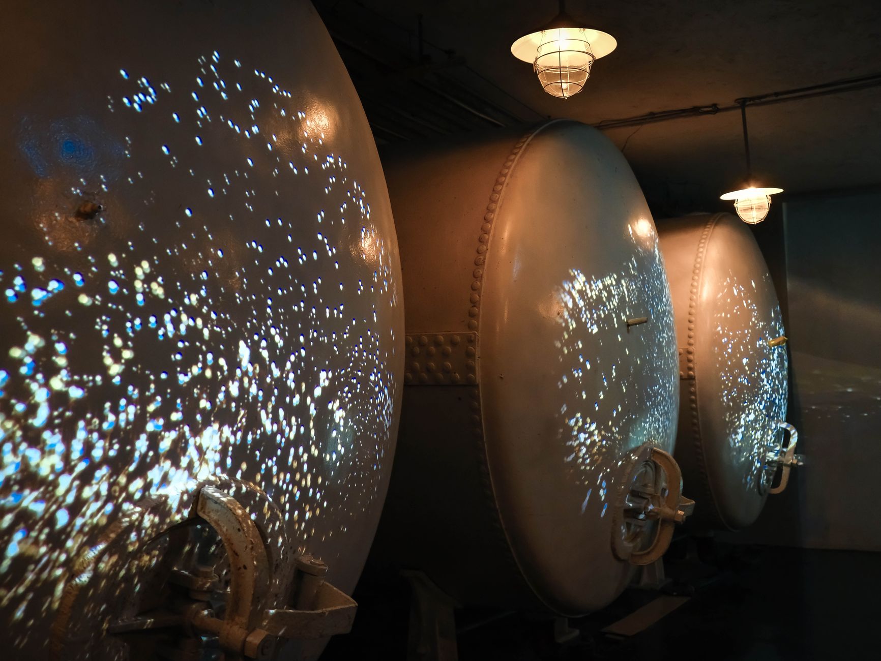 Dimly lit industrial wine fermentation tanks with unique light reflections creating a futuristic atmosphere.