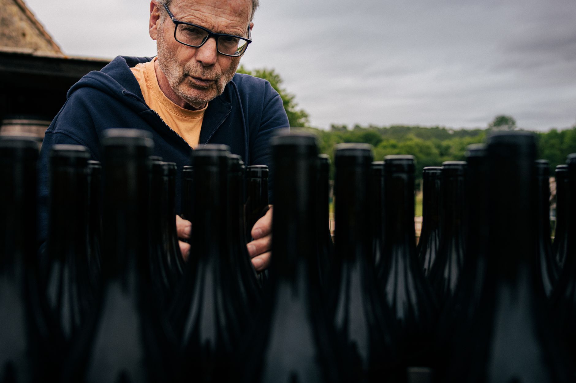 Winemaker examines bottles in an outdoor vineyard setting in Nouvelle-Aquitaine, France.