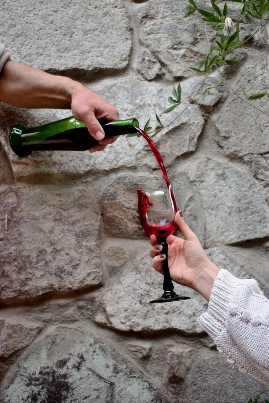 Close-up of red wine being poured into a glass against a stone wall.
